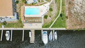 An aerial view of a waterfront property with a swimming pool, docked boats, and a covered patio area.
