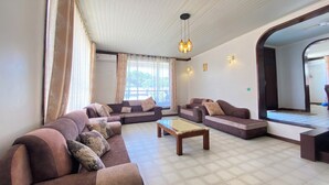 A spacious living room with a large sofa set, a coffee table, and a view of the outdoors through large windows. - Jim Holiday Homes (Mombasa)