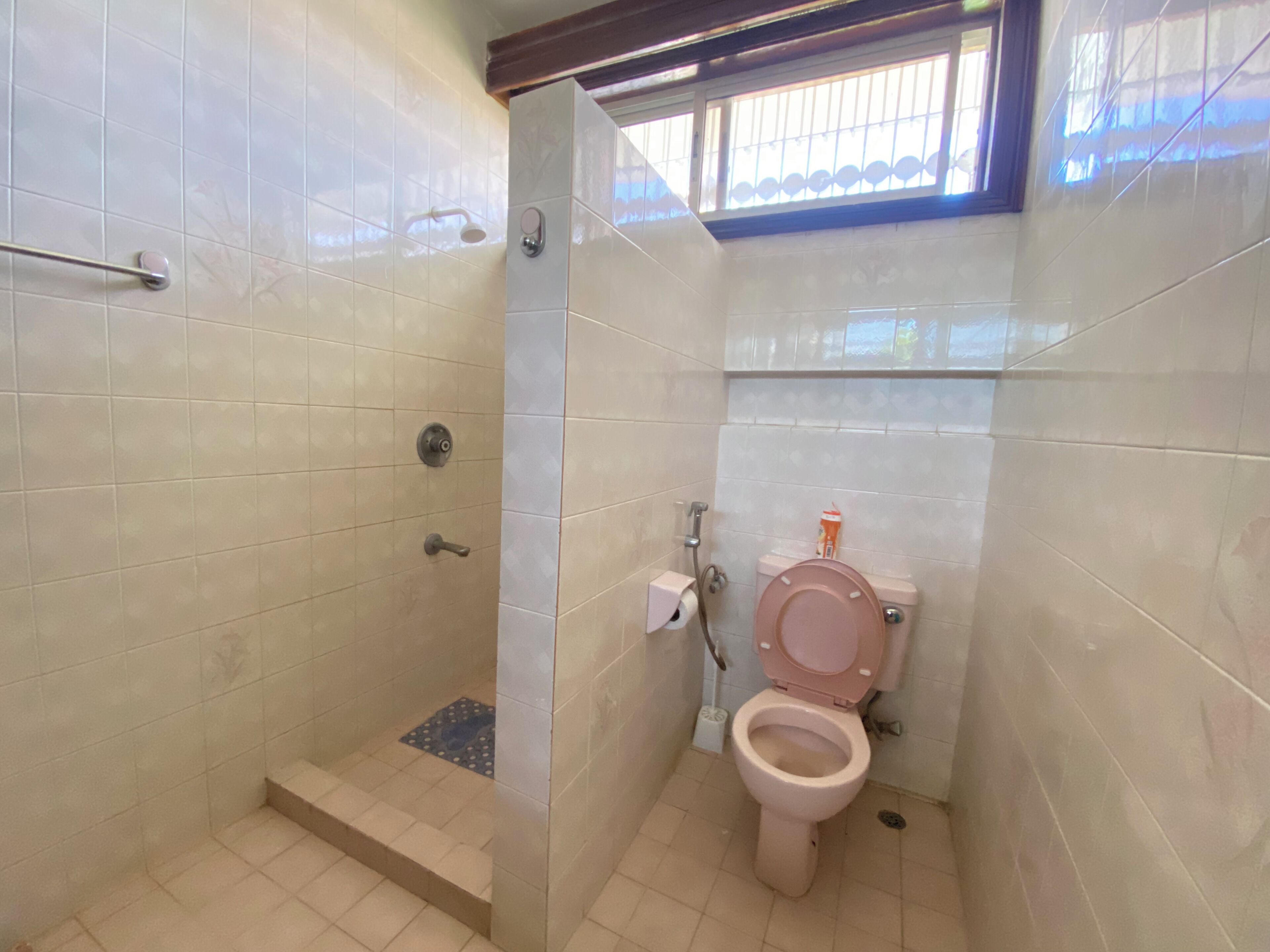 A small bathroom with a toilet, a shower, and a window.
