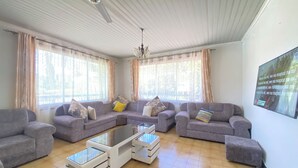 A spacious living room with a sectional sofa, a glass coffee table, and a ceiling fan. - Jim Holiday Homes (Mombasa)