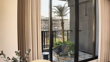 Habitación moderna con una mesa de madera y una planta en maceta, puertas de vidrio correderas que dan a un espacio exterior con plantas y una palmera.