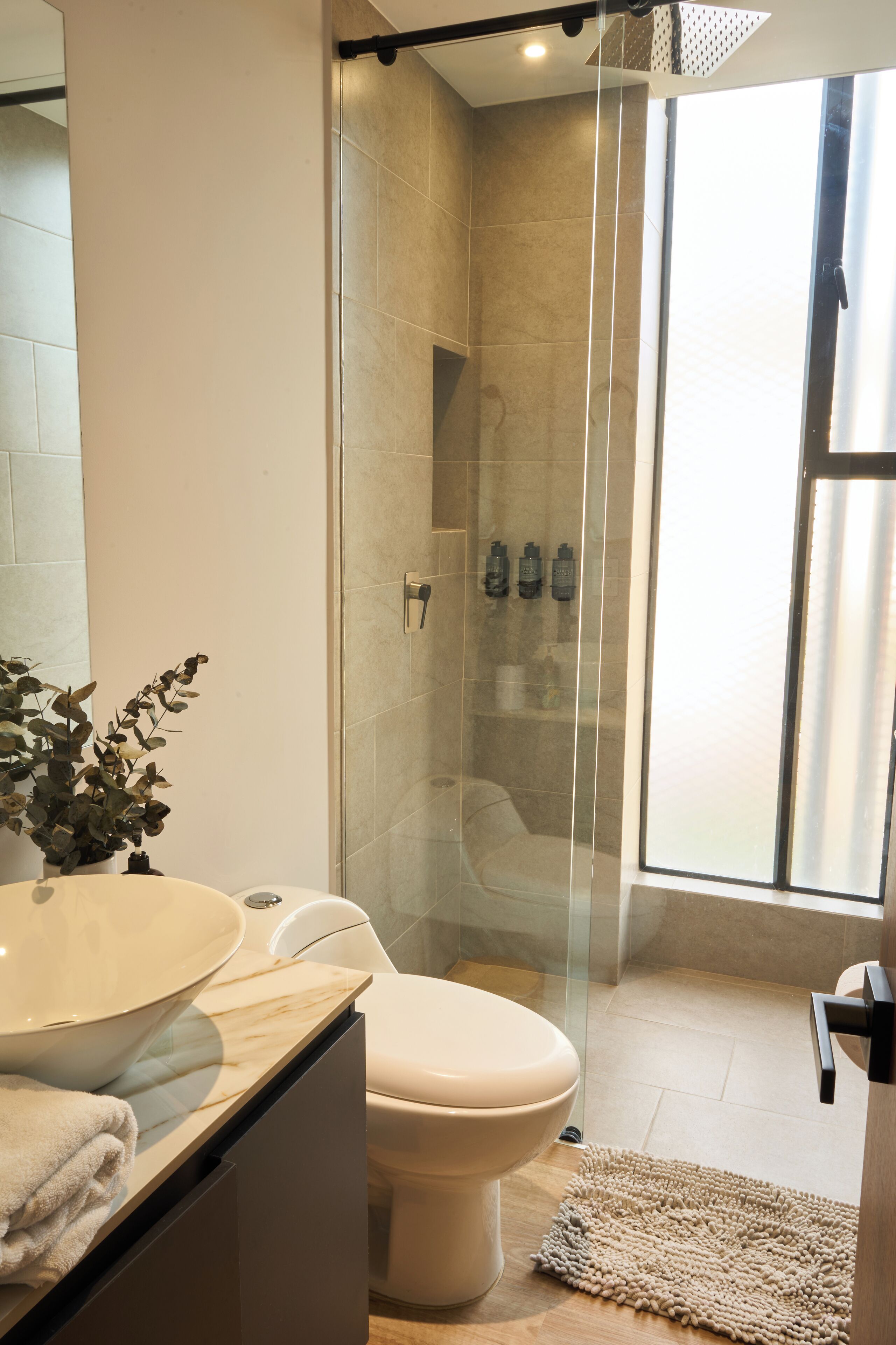 A modern bathroom with a glass-enclosed shower, a marble sink, and a toilet.