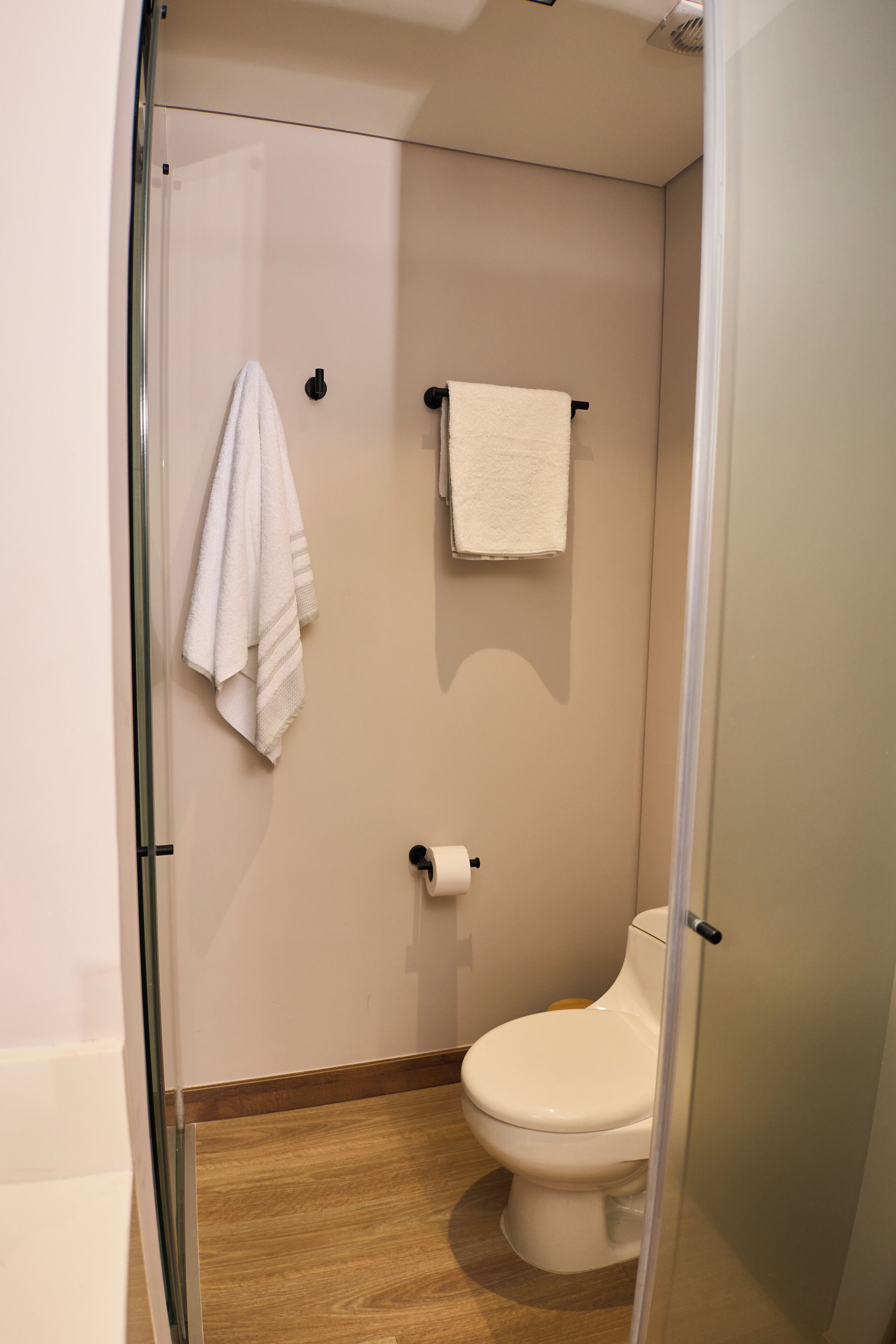 Een kleine, praktische badkamer met toilet, een handdoekhouder en een douchehoek.