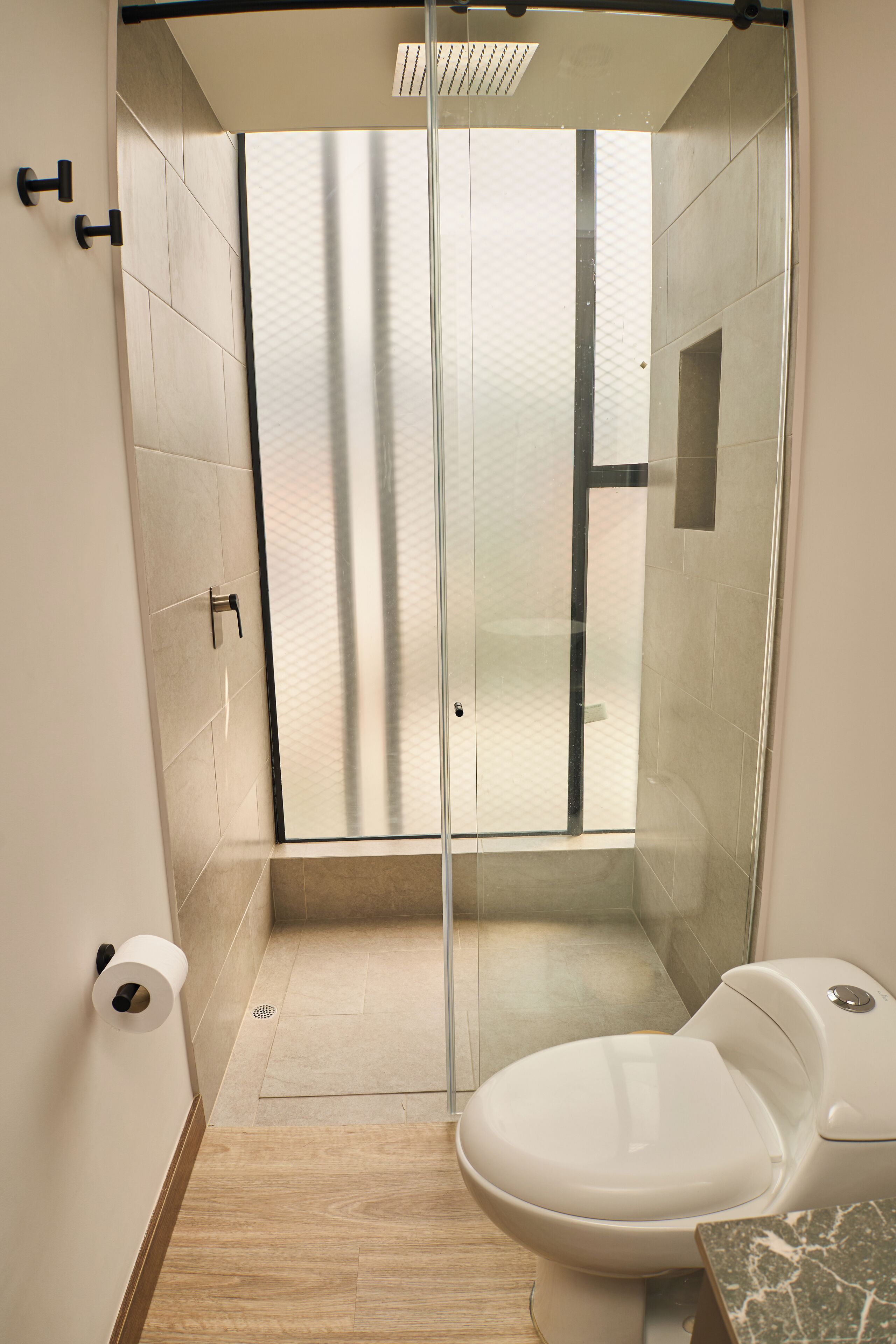 Un baño moderno con cabina de ducha de vidrio, inodoro y encimera de mármol.