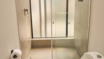 Un baño moderno con cabina de ducha de vidrio, inodoro y encimera de mármol.