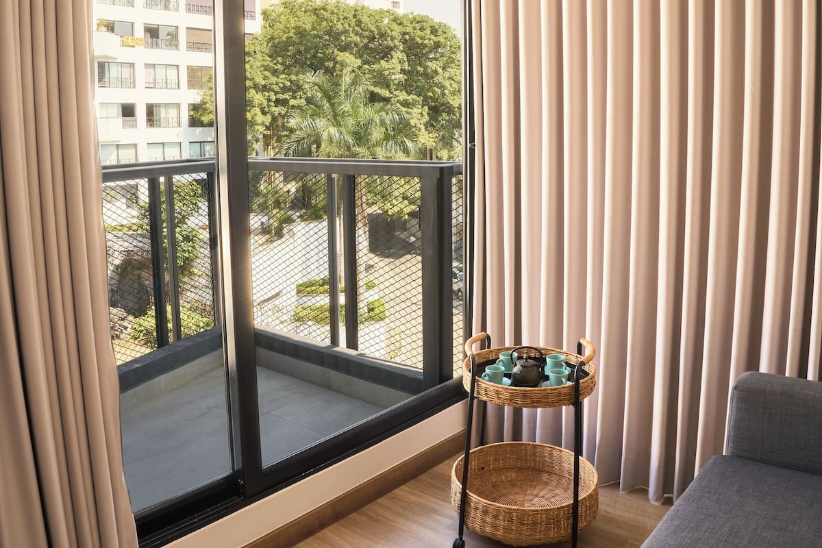 A modern room with a large window, a grey sofa, a wicker side table, and a view of a cityscape.