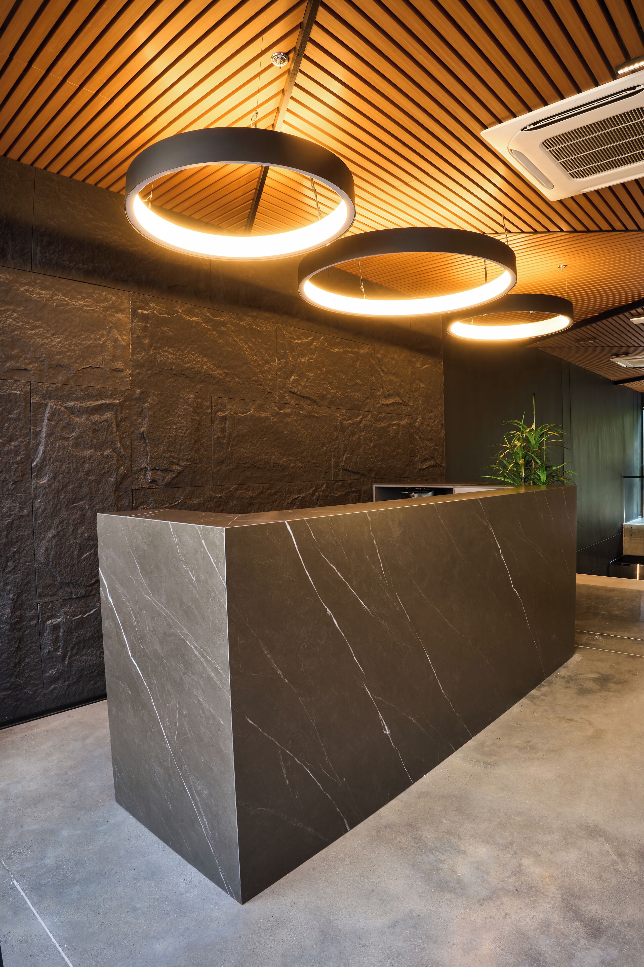 Zona de recepción con mostrador de mármol, techo de listones de madera e iluminación colgante circular.
