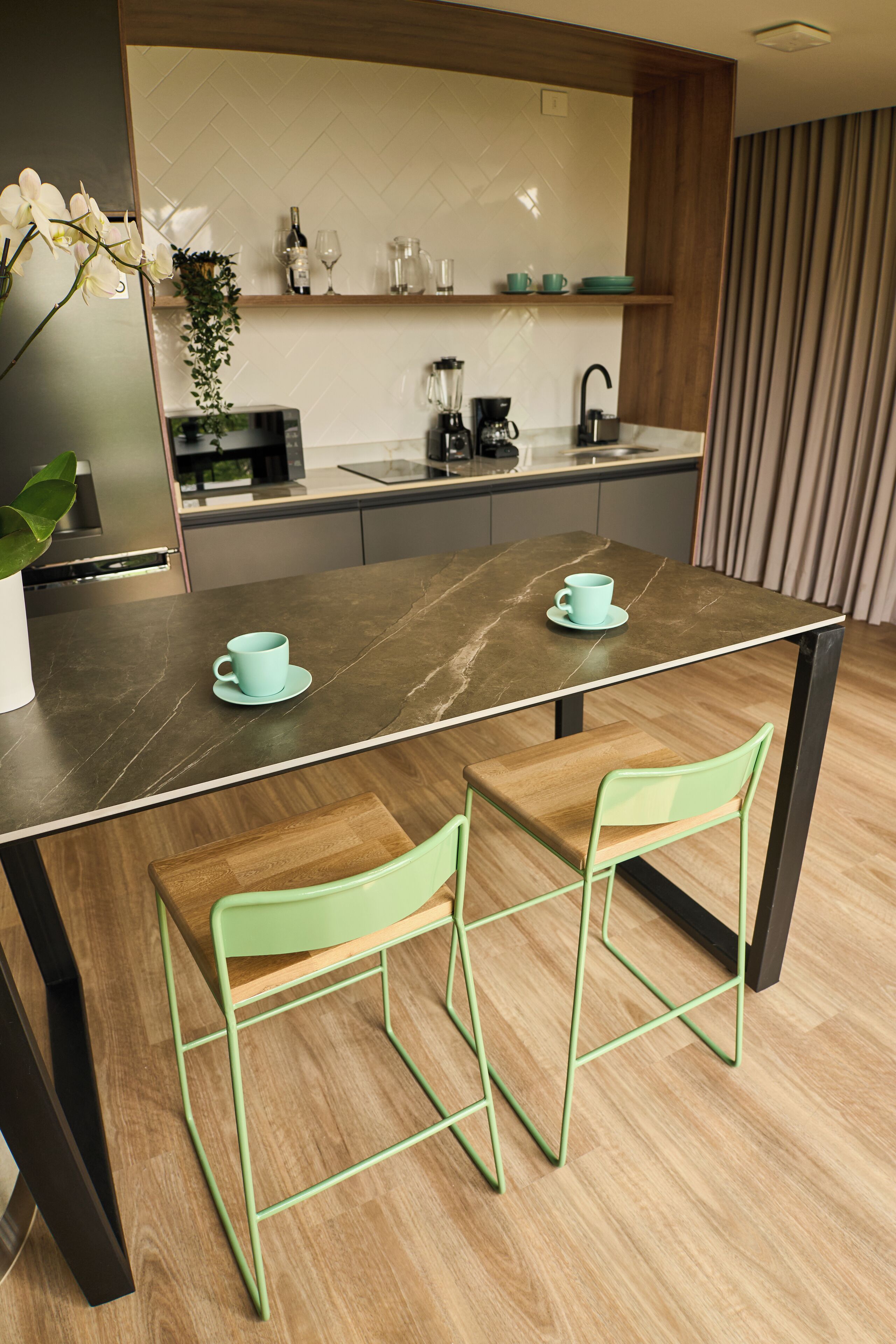 Een moderne keuken met een donker marmeren aanrecht, twee groene stoelen en een koffieapparaat.