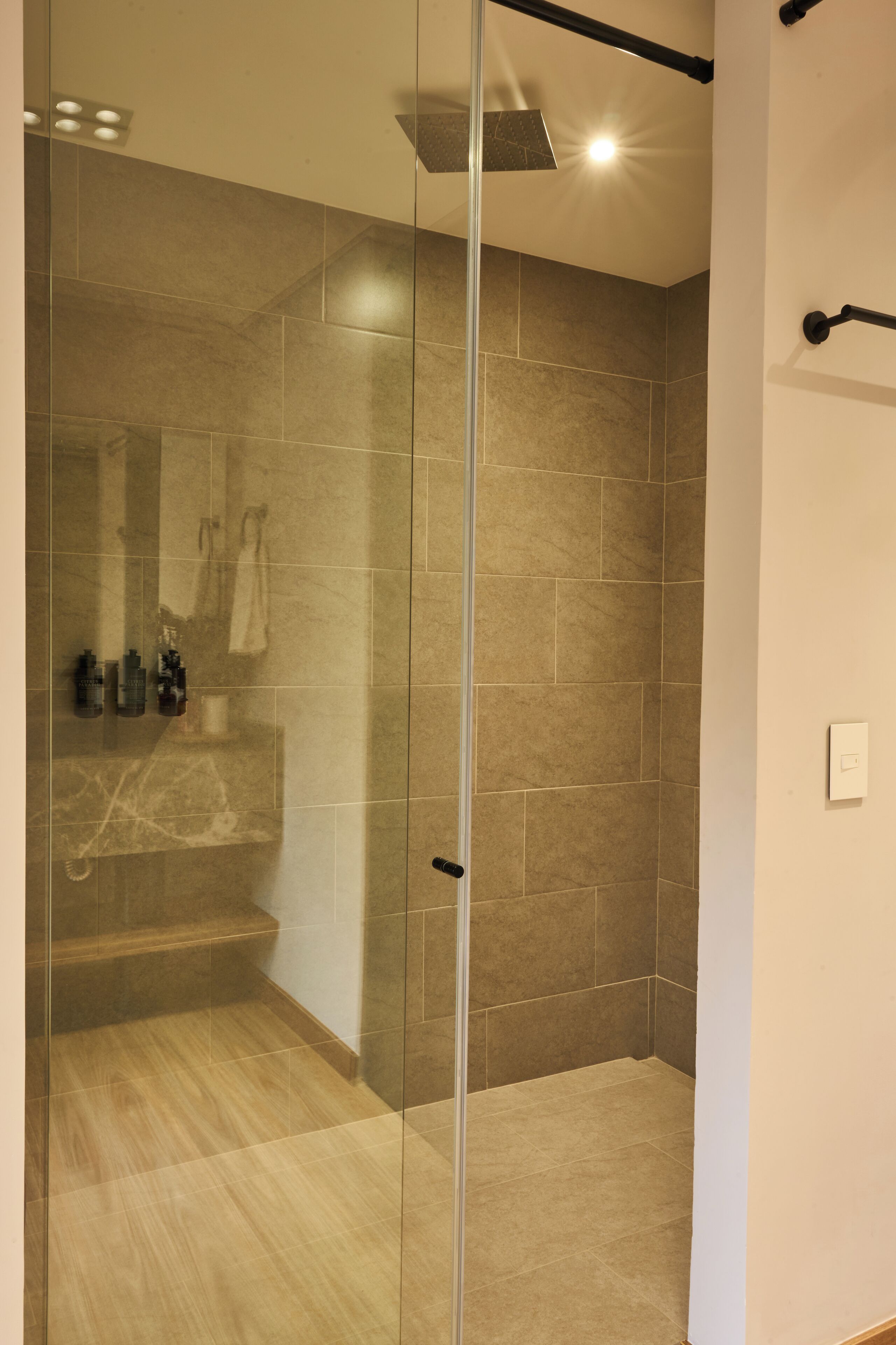 Un baño moderno con cabina de ducha de vidrio, paredes con azulejos y suelo de madera.