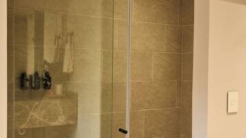 Un baño moderno con cabina de ducha de vidrio, paredes con azulejos y suelo de madera.