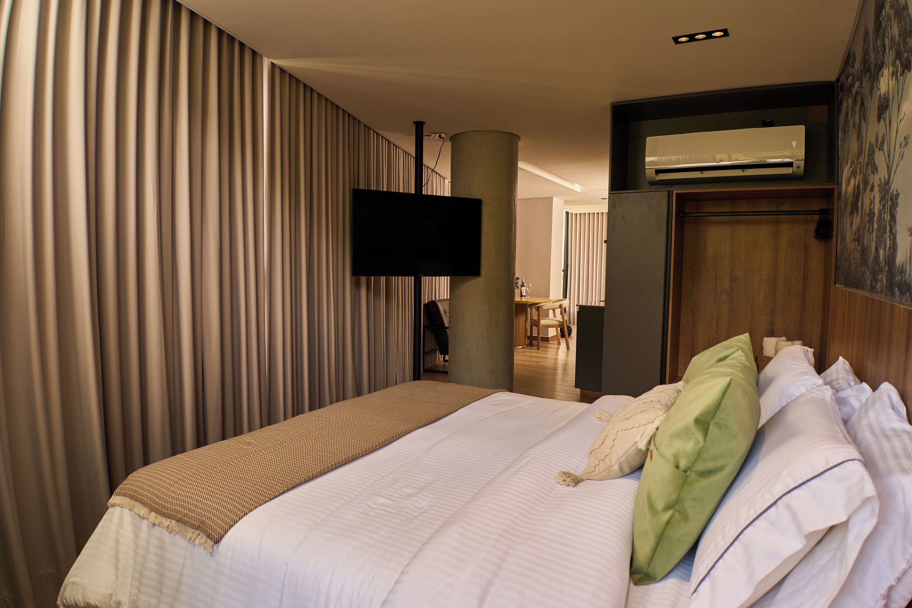 Een hotelkamer met een groot bed, een flatscreen televisie aan de wand en een airconditioning boven het bed.