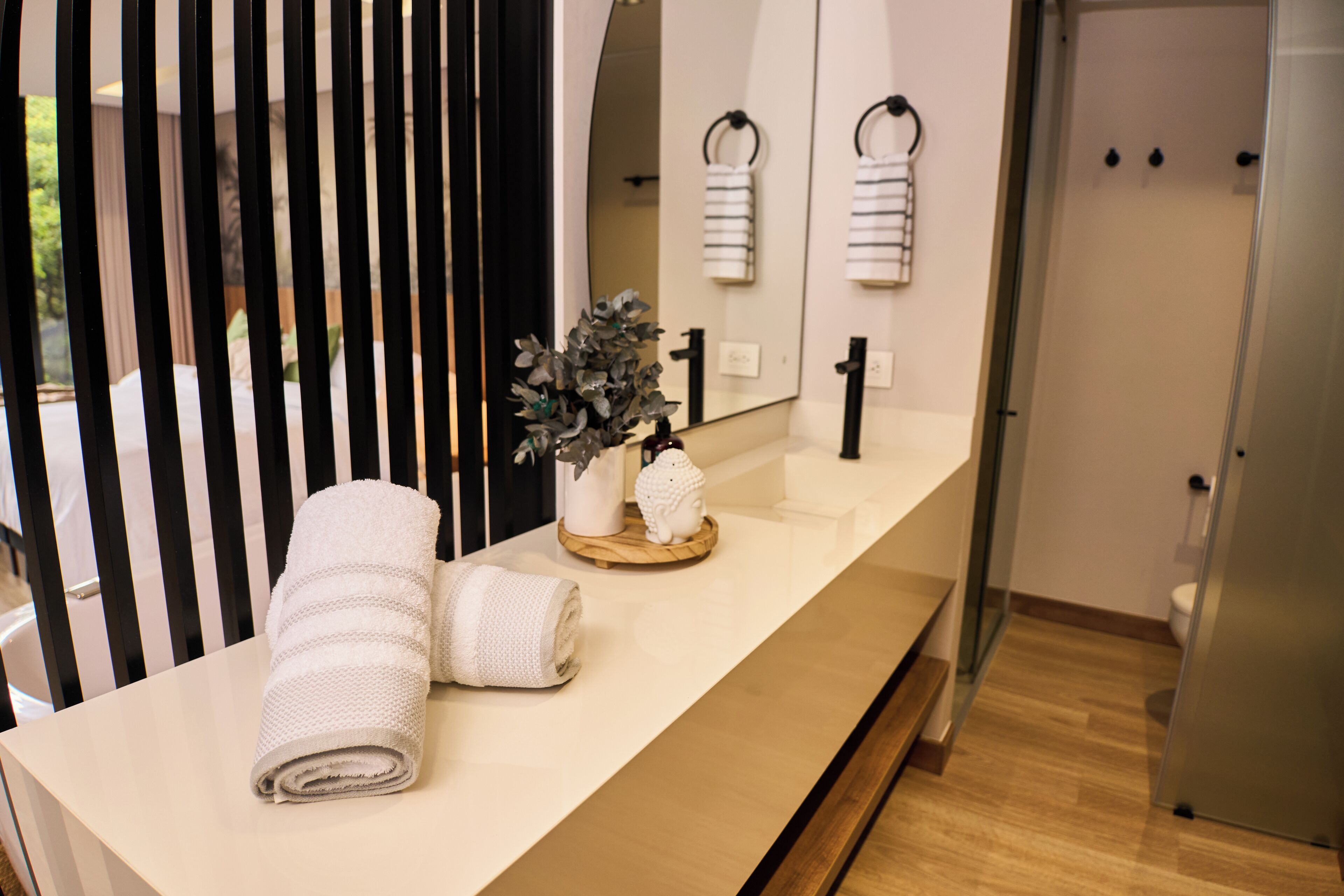 Un baño con encimera blanca, espejo, toalla y planta decorativa.