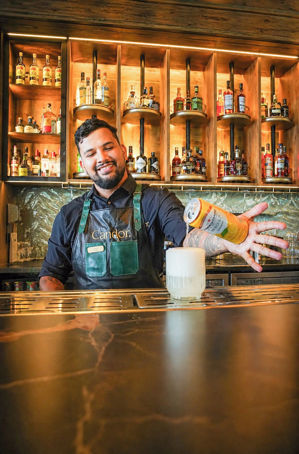 Un cantinero detrás de una barra con estantes llenos de botellas de licor.