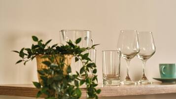 A wooden shelf with a clear glass pitcher, two wine glasses, and a green cup.