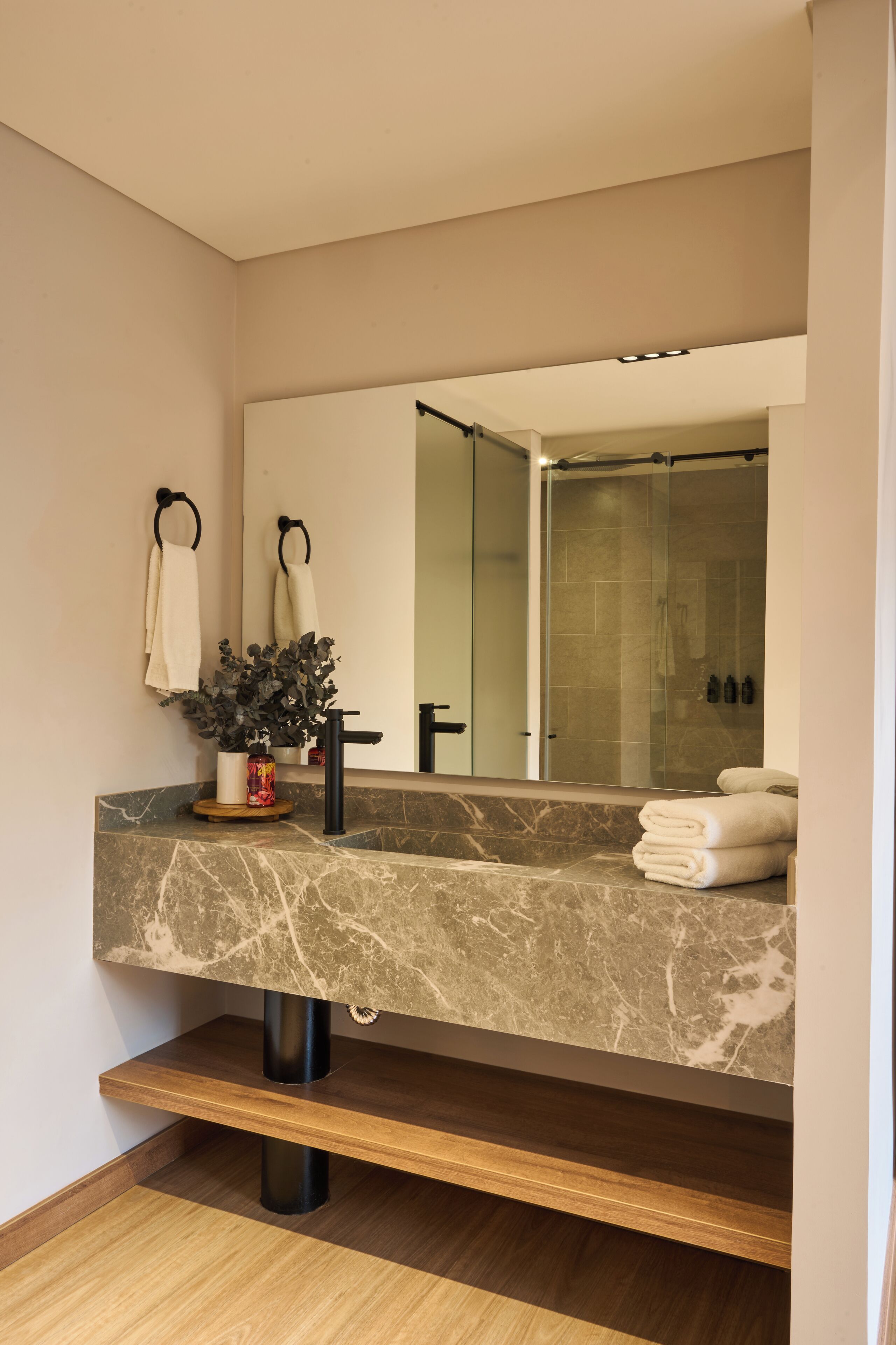 Un baño moderno con lavamanos de mármol, un espejo grande, una planta en maceta y una cabina de ducha de vidrio.