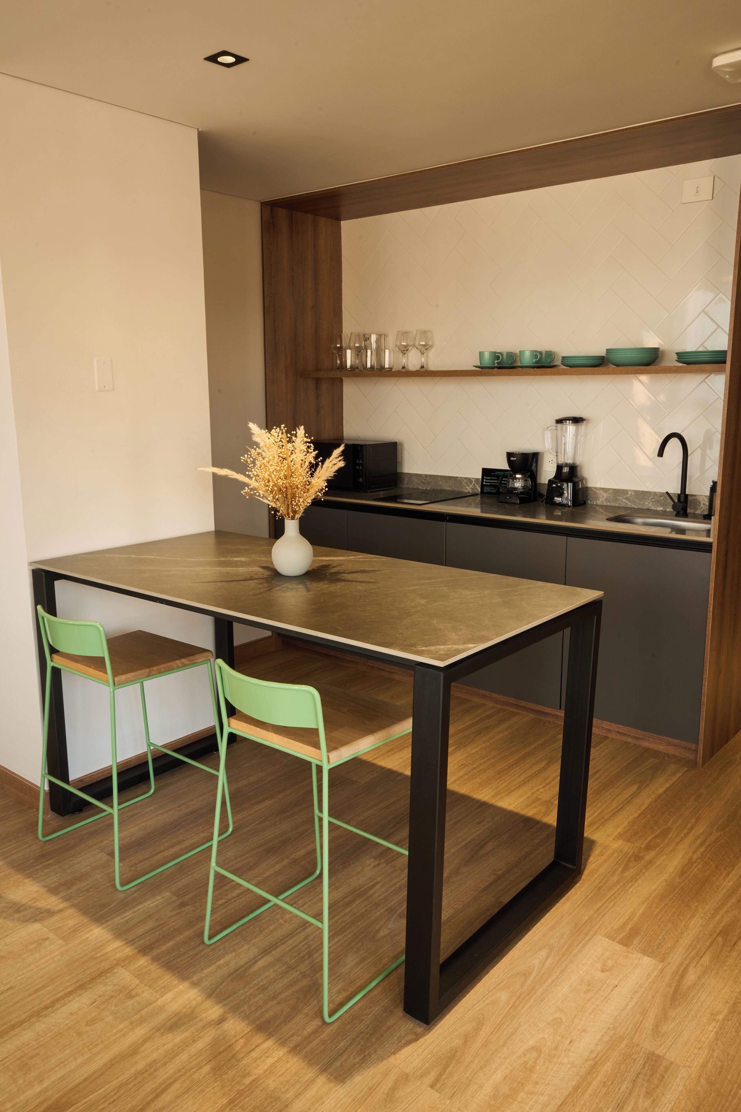 Una cocina moderna con una mesa y sillas de madera, una cafetera y un jarrón con flores secas.