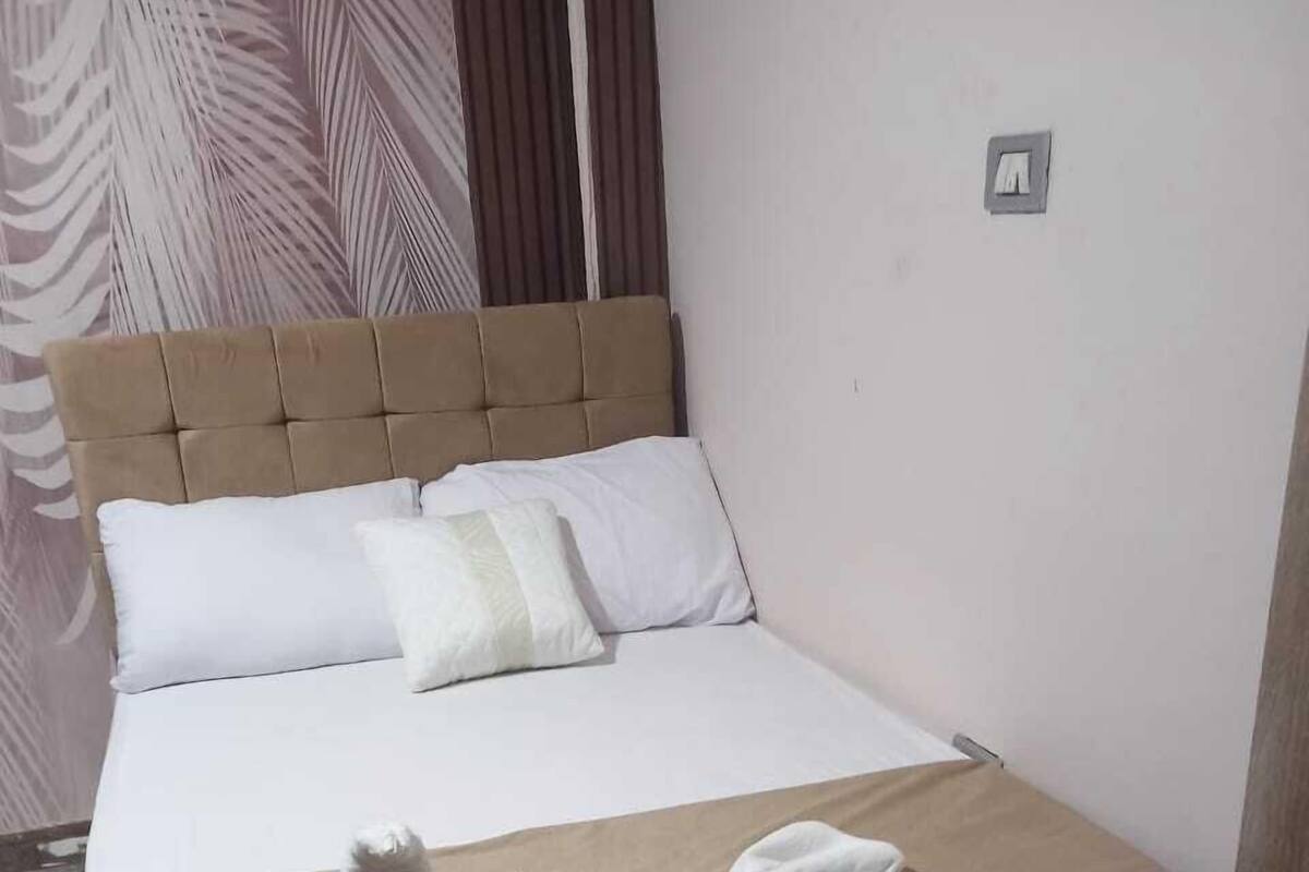 A neatly made bed with a beige headboard and white bedding, a white towel, and a fluffy white pillow on the bed.
