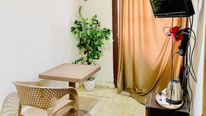 A small room with a table, two chairs, a potted plant, an air conditioner, a TV, and a coffee maker. - Narmar Hotel (Giza)