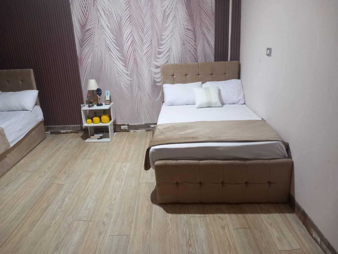 A hotel room with a large bed, a bedside table with a lamp, and a small shelf with decorative items.