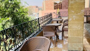A terrace with wicker furniture and a decorative metal railing, featuring a view of buildings and trees in the background. - Narmar Hotel (Giza)