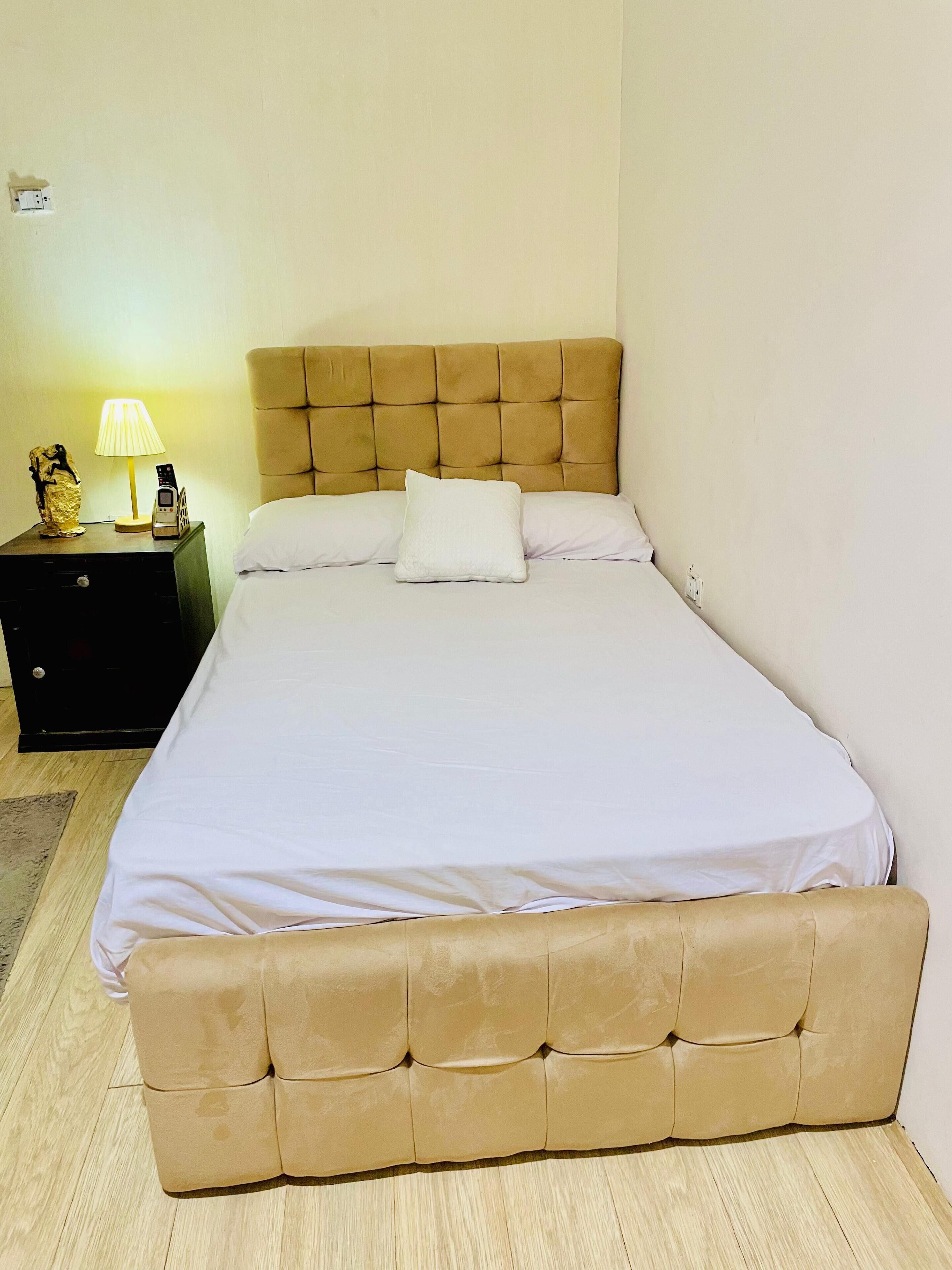 A neatly made bed with a tufted headboard, a bedside table with a lamp, and a small decorative item.