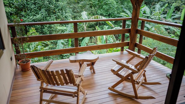 Eine Holzterrasse mit zwei Schaukelstühlen und einem kleinen Tisch, umgeben von üppigem Grün.