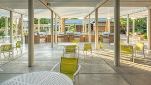 An outdoor patio area with round tables and chairs, a barbecue grill, and a stone wall.