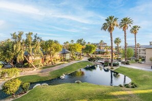 A landscaped area with a pond, palm trees, and a building with a blue roof. - Indio | Mobility-Friendly Resort Stay | Desert Sun & Pools | Accessible Studio (Indio)