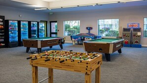 Une salle avec deux tables de baby-foot, une table de billard et des distributeurs automatiques.