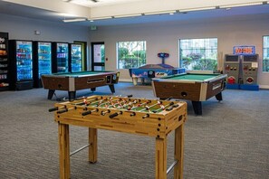 A room with two foosball tables, a pool table, and vending machines.