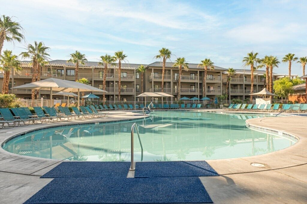 A hotel with a large pool, sun loungers, and palm trees.