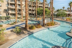 A hotel pool area with multiple levels of balconies, palm trees, and lounge chairs.