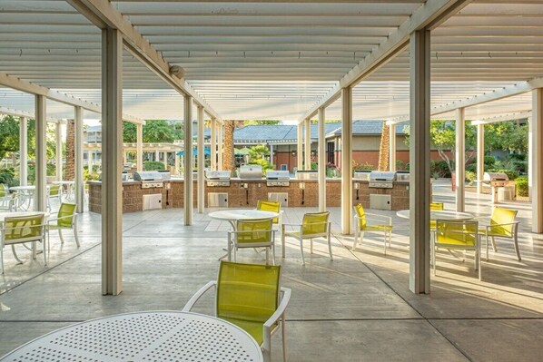An outdoor patio area with round tables and chairs, a barbecue grill, and a stone wall.