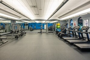 A gym with various exercise equipment, including treadmills, weight machines, and a mirrored wall.