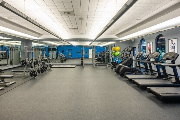 A gym with various exercise equipment, including treadmills, weight machines, and a mirrored wall.