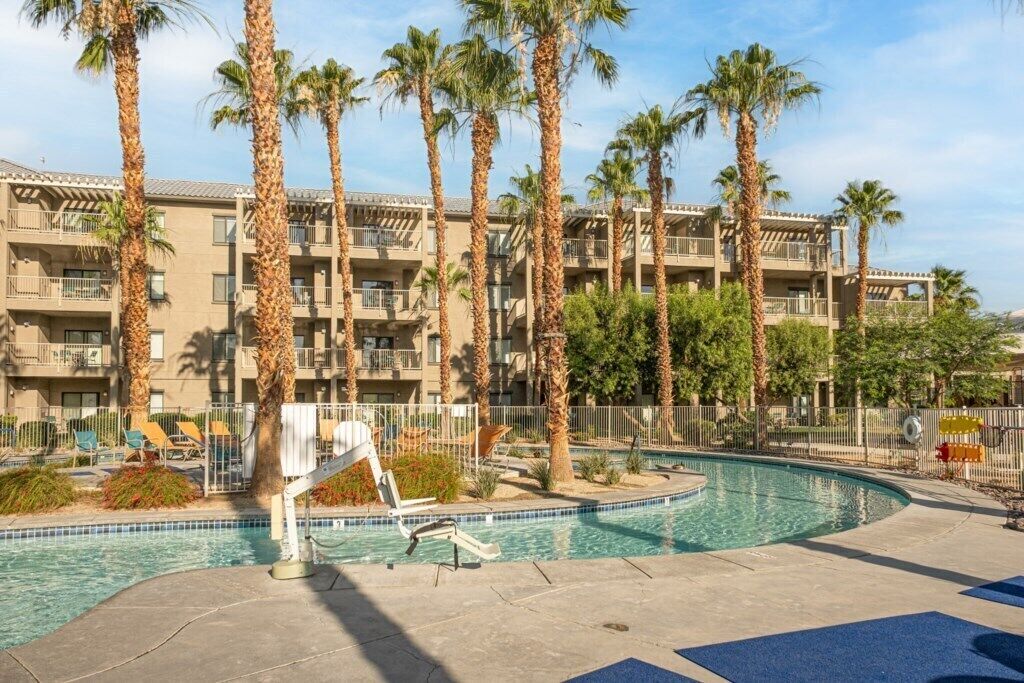 Un hôtel doté d’une piscine entourée de palmiers et de chaises longues.