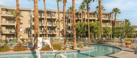 Un hotel con piscina rodeada de palmeras y sillas de descanso.