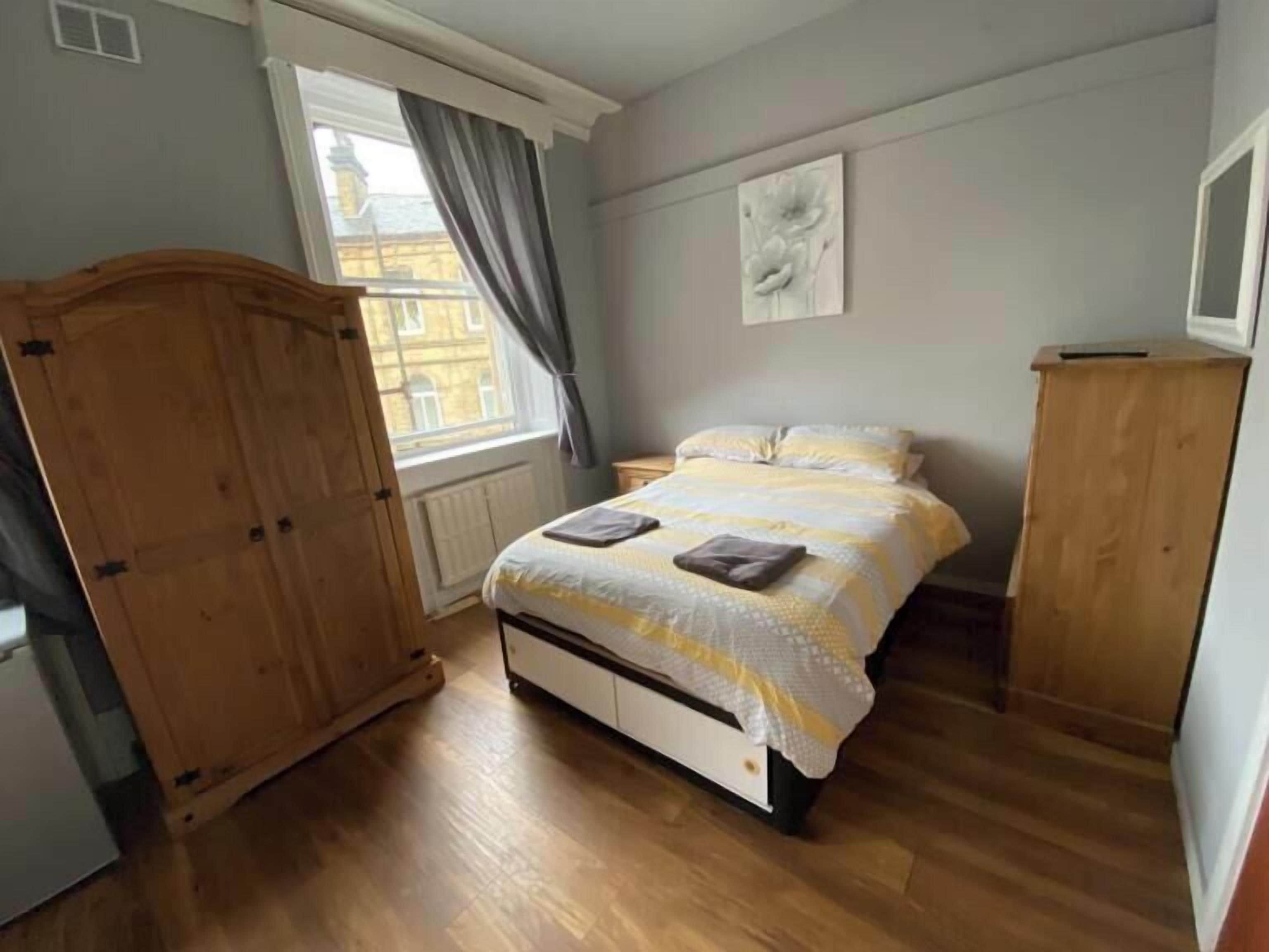 A bedroom with a bed, wooden wardrobe, and a window with curtains.