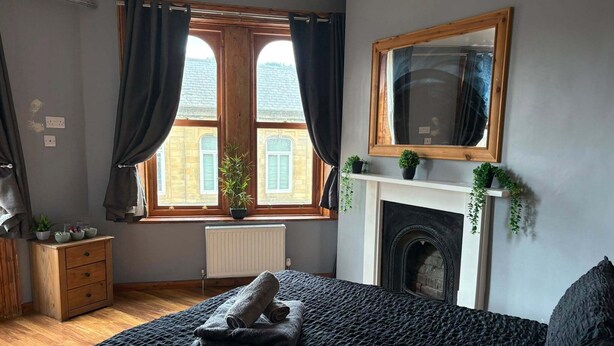 Een slaapkamer met een bed, een raam met gordijnen, een openhaard en een spiegel aan de muur.