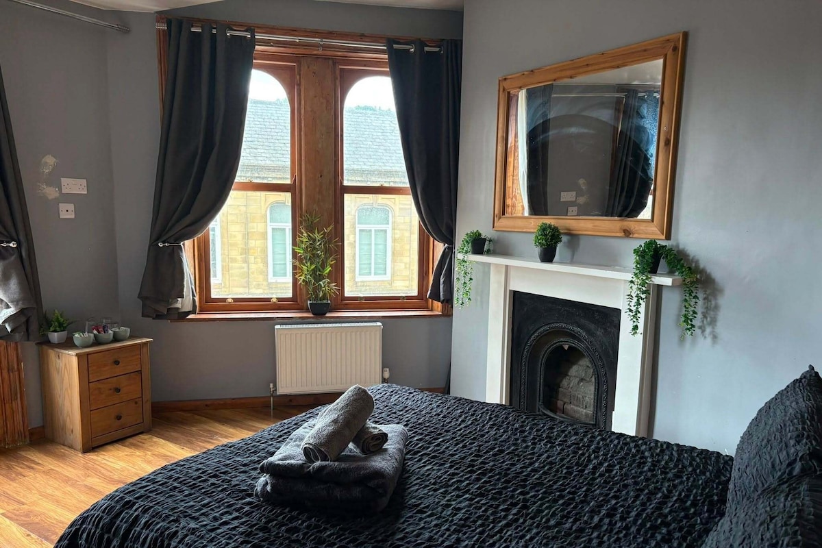 Un dormitorio con cama, ventana con cortinas, chimenea y un espejo en la pared.