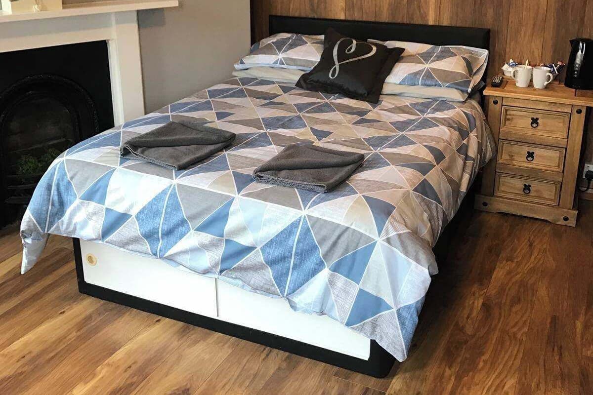 Een slaapkamer met een bed, een open haard, een nachtkastje en een wandlamp.