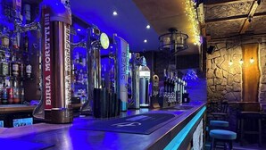 Een bar met een toog, diverse flessen en een stenen muur.