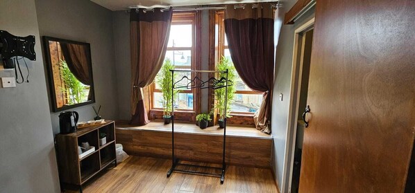 A room with a wooden floor, a window with curtains, a drying rack, and a shelf with items. - THE BULL ON THE BRIDGE (Sowerby Bridge)