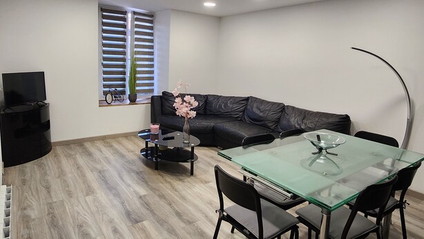 A modern living room with a glass dining table, black leather sofa, and a TV stand. - Town house located in LONGNES (Yvelines) (Longnes)
