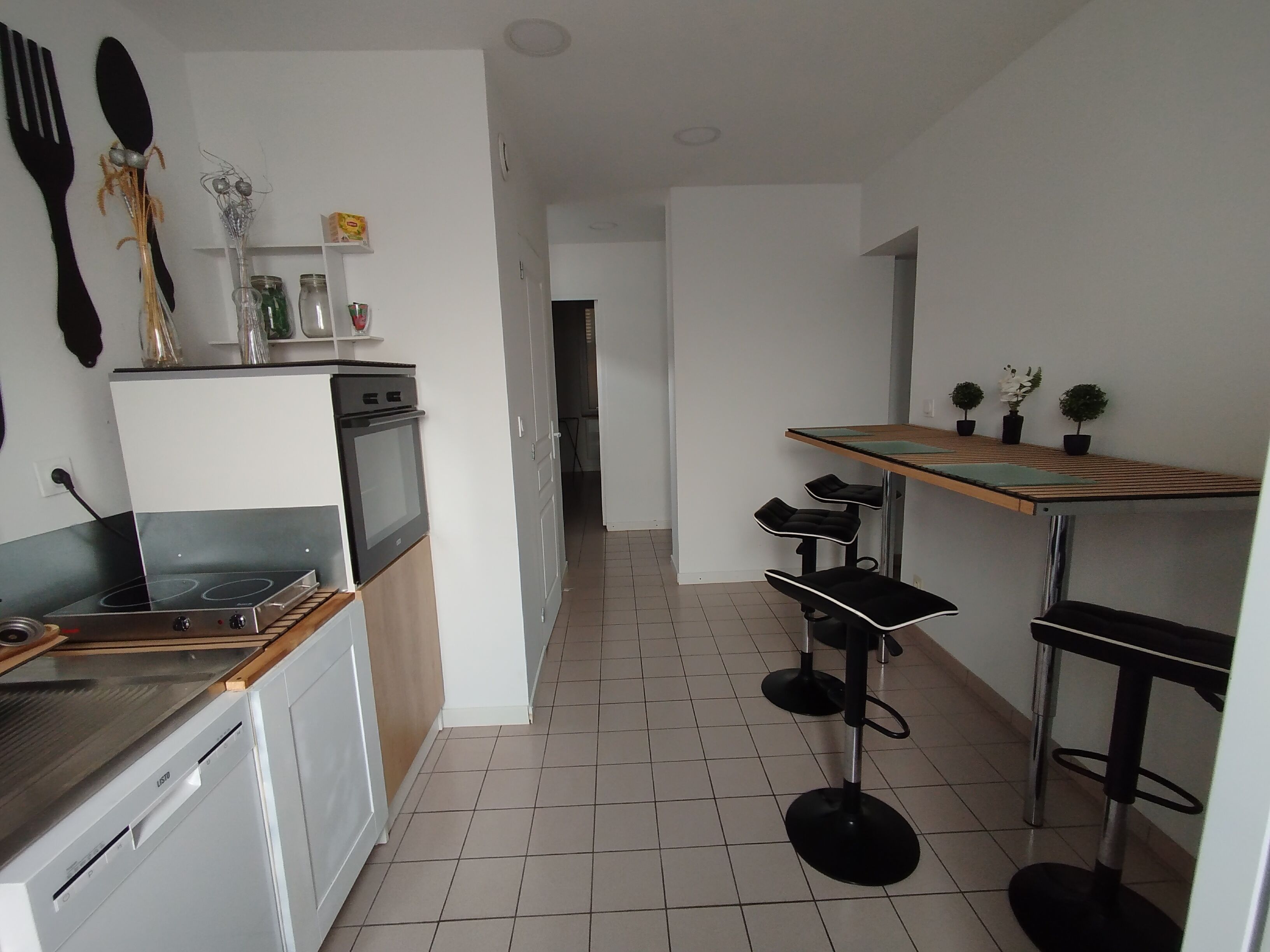 A modern kitchen with a built-in oven, a dishwasher, and a small dining area with a table and chairs.
