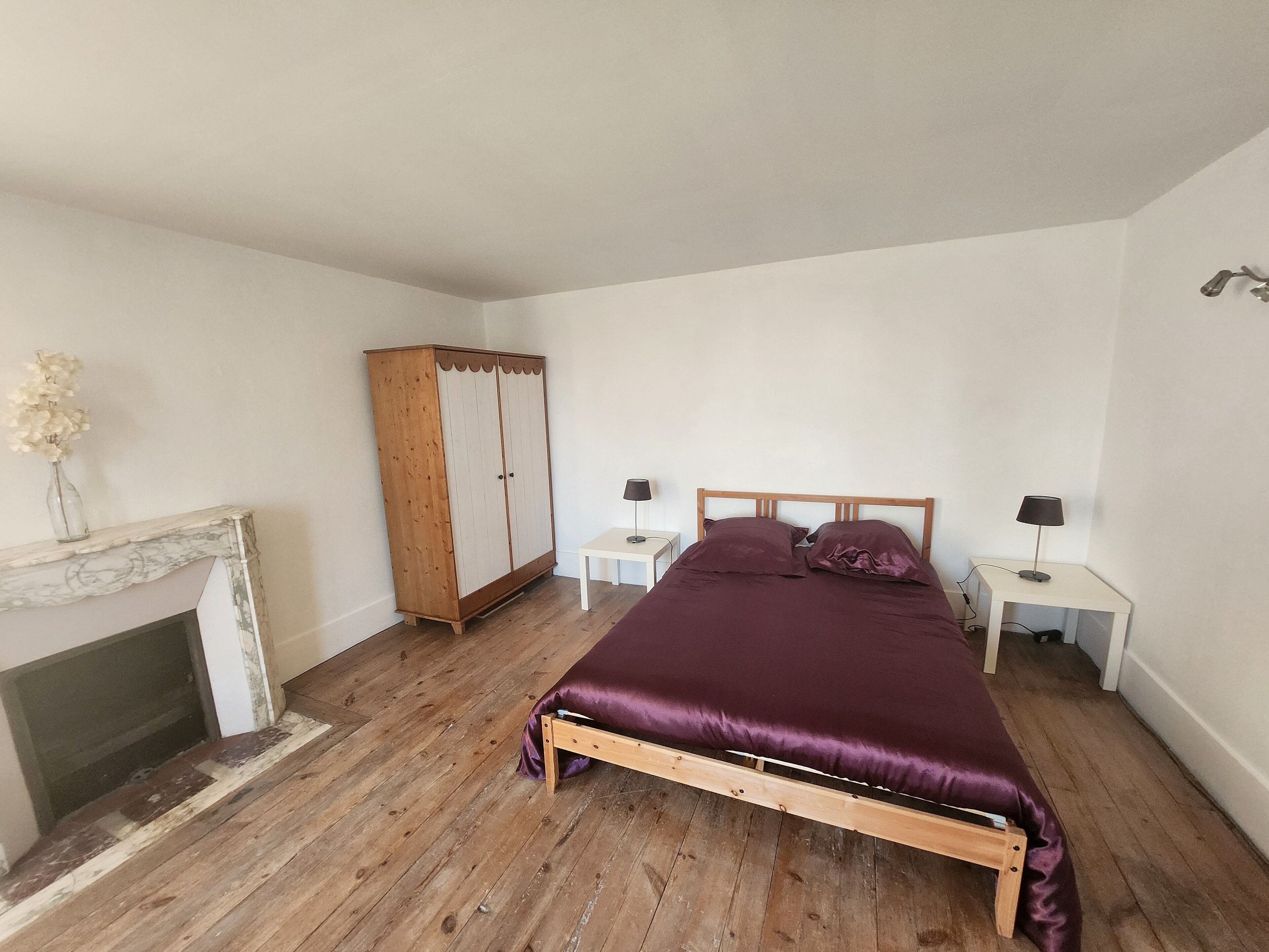 Un dormitorio con una cama de madera, dos mesitas de noche con lámparas, un armario de madera y una chimenea.