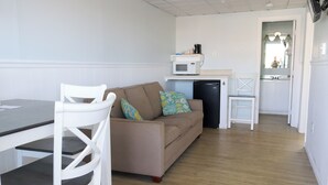 A compact living space with a kitchenette, a dining area with a table and chairs, and a sofa with patterned cushions. - Mainsail Inn & Cottages (Hampton)
