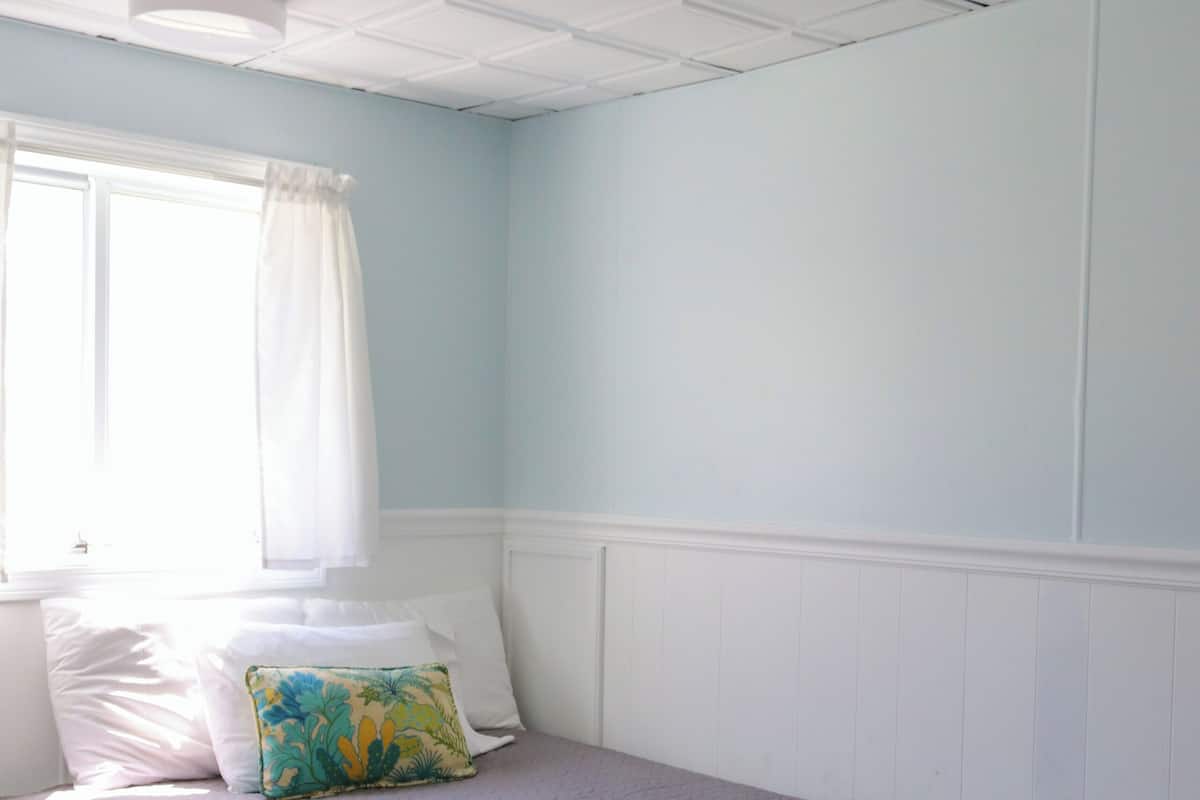 A neatly made bed with a brown quilt, white headboard, and a single decorative pillow.