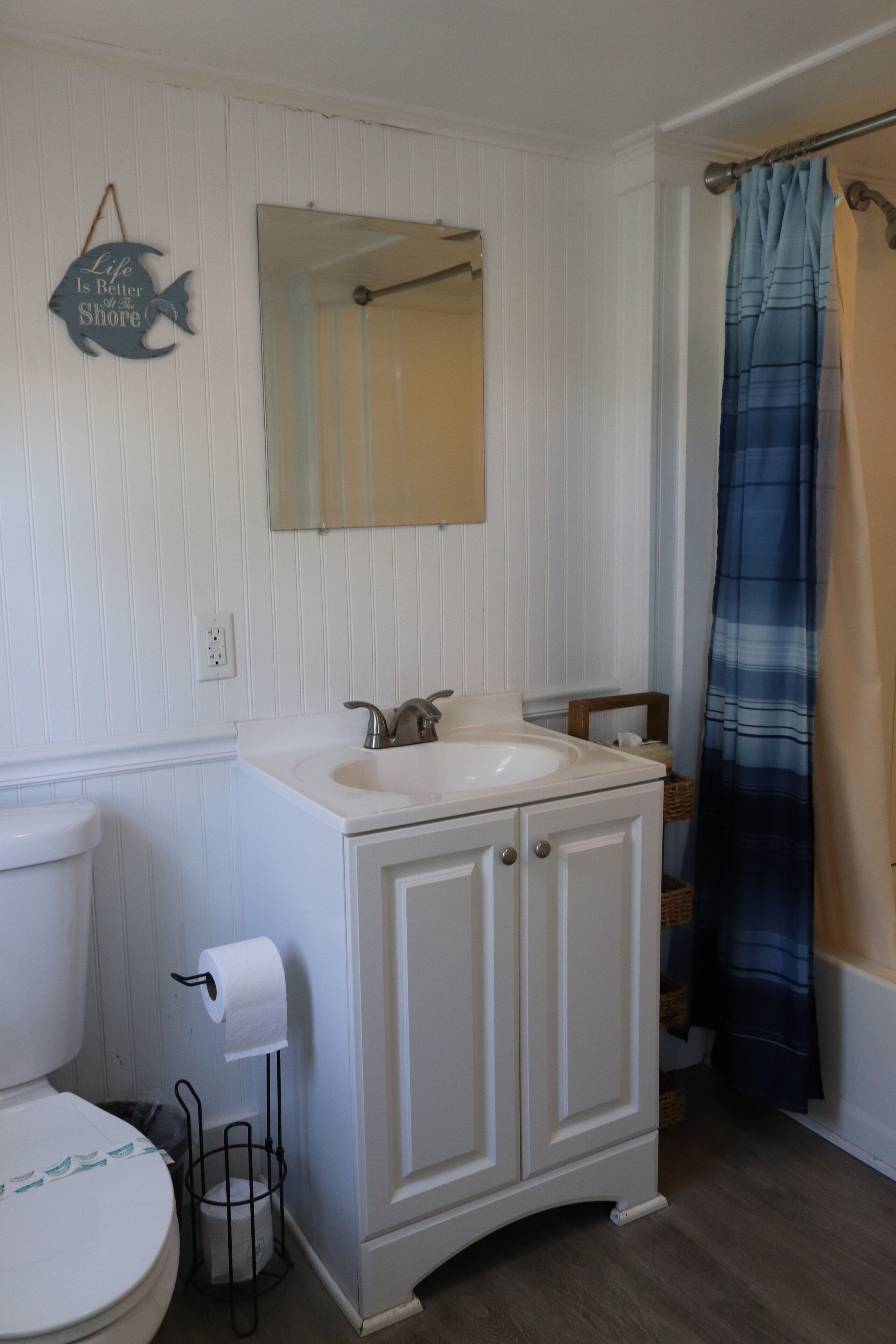 A bathroom with a white vanity, a mirror, a toilet, and a blue-striped shower curtain.