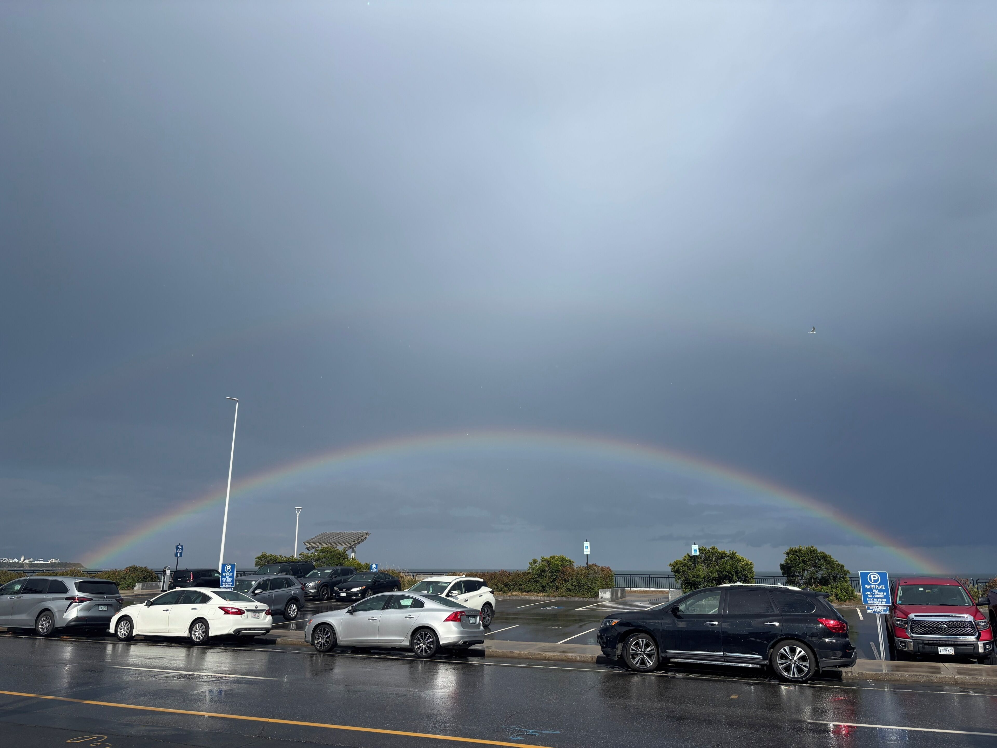 A parking lot with cars and a visible rainbow.